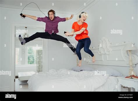 Playful Couple Jumping On Bed And Listening To Music With Mp3 Player