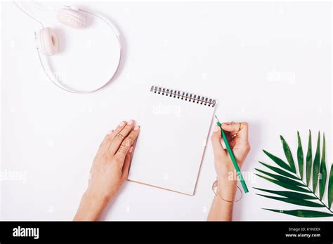 Female Hands Write In A Notebook Headphones And Green Leaf On White