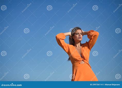 Young And Beautiful Woman In An Orange Dress With Her Hands On Her Head In Sensual Attitude