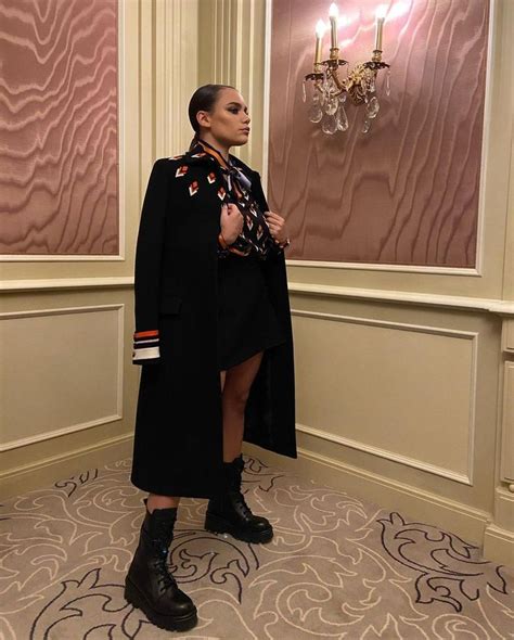 A Woman Standing In Front Of A Chandelier Wearing A Black Coat And Scarf