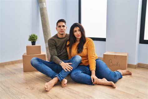 Young Couple Sitting On The Floor At New Home Relaxed With Serious