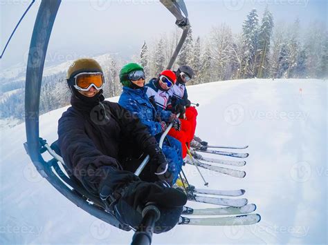Cheerful young friends skiers on ski lift ride up on ski slope at snowy