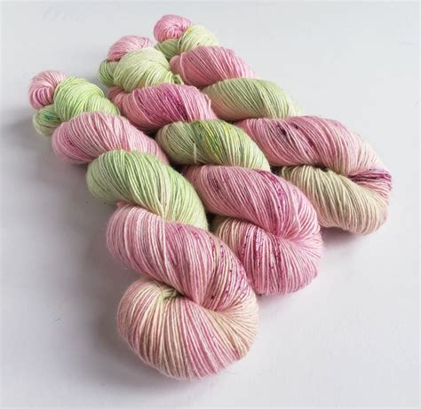 Several Skeins Of Pink And Green Yarn On A White Surface