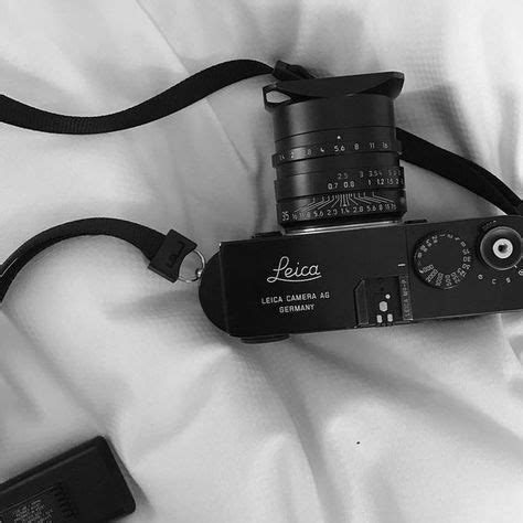 A Black And White Photo Of A Camera On A Bed With A Strap Around It S Neck