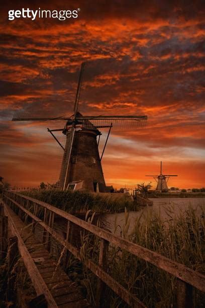 Majestic Windmill Atop A Grassy Field Under A Glowing Sunset Sky In