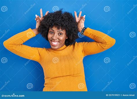 Black Woman With Curly Hair Standing Over Blue Background Posing Funny And Crazy With Fingers On