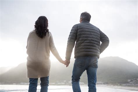 Vista traseira do casal de mãos dadas na praia Foto Premium