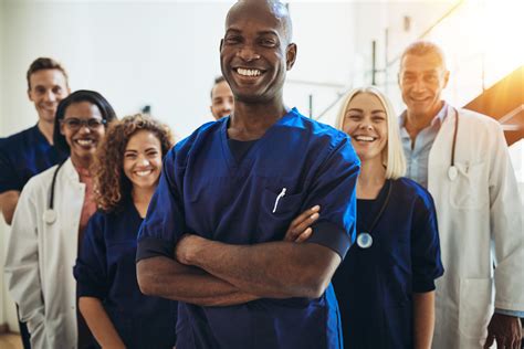 Smiling African Doctor Standing In A Hospital With His Staff Online