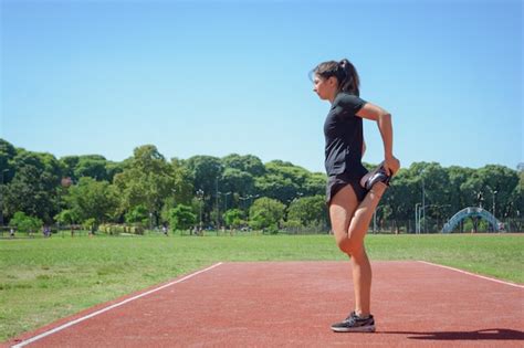 Vista Lateral De La Joven Mujer Latina De Pie En La Pista De Atletismo Estirando La Pierna Del