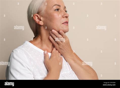 Mature Woman Doing Thyroid Self Examination On Beige Background Stock