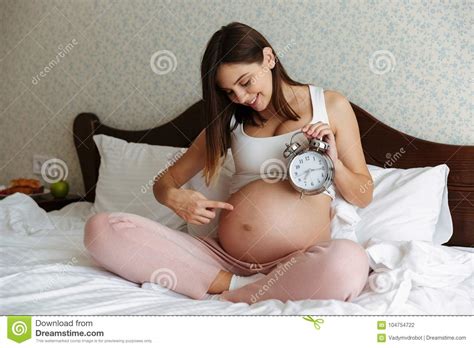 Femme Enceinte Gaie S Asseyant Sur Le Lit Tenant L Alarme Photo Stock