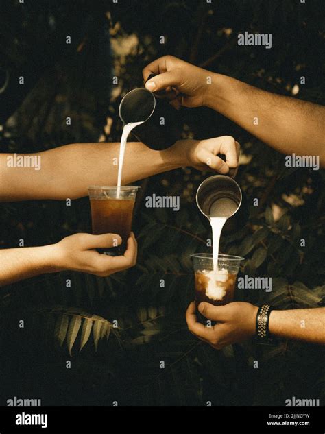 A Vertical Of Two Baristas Pouring Milk Into The Plastic Cups Filled