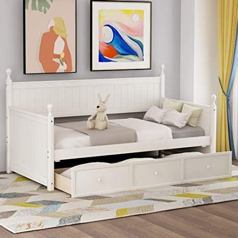 a white bed with two drawers underneath it in a living room next to a ...