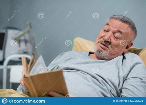 A Handsome Senior Man Reading A Book In Bed At The Hospital Ward Stock