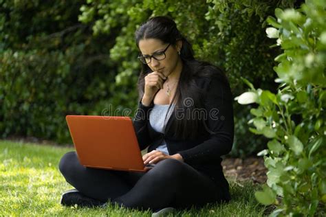 A Young Brunette Woman Is Sitting On The Grass Of A Park With Her