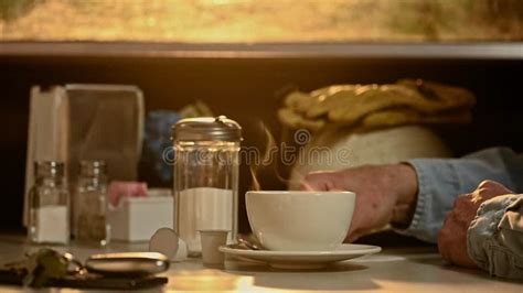 A Construction Worker Adding Sugar To His Steaming Hot Cup Of Coffee In A Diner At Sunrise Stock