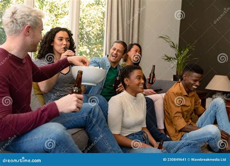 Group Of Happy Diverse Female And Male Friends Watching Tv And Drinking