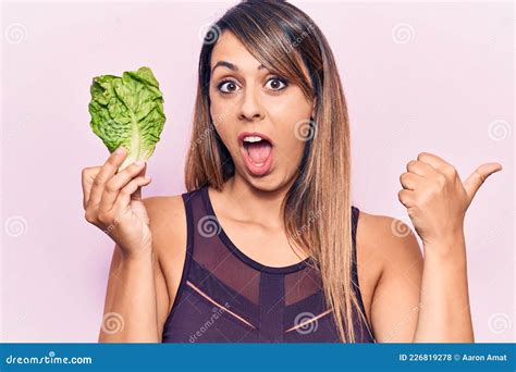 Young Beautiful Woman Holding Lettuce Pointing Thumb Up To The Side