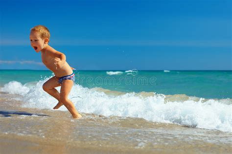 El Niño Lindo Que Se Ejecuta Del Mar Agita En La Playa Foto de archivo