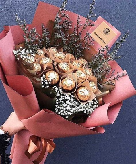 A Bouquet Of Flowers With Chocolates Wrapped In Pink Paper And Tied To