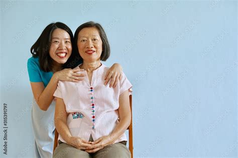 Senior Asian Mother Sitting On The Chair With Asian Young Daughter With Smiling Face Holding Her