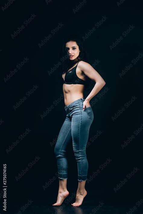 Sexy Brunette Barefoot Woman In Blue Jeans And Bra Posing With Hands In Pockets Isolated On
