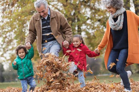 Playful Grandparents And Grandchildren Kicking Autumn Leaves In Park