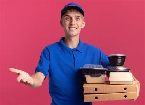 Souriant jeune livreur blonde garde la main ouverte et détient des contenants de nourriture et