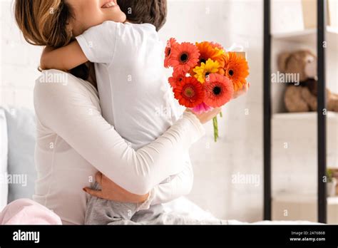 Cropped View Of Happy Mother Hugging Son While Holding Flowers On