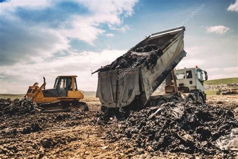 Dumping truck unloading garbage at dumping site. Industrial bulldozer, excavator and dumping ...