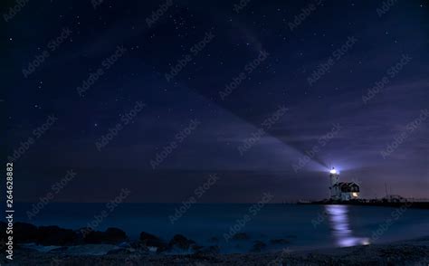 Lighthouse shining beam of light into the night sky over blue lake as a ...