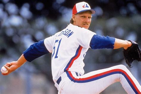 A Baseball Player Pitching A Ball On Top Of A Field With Trees In The