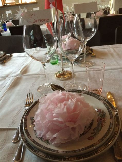 A Table Set With Plates Silverware And Pink Tissue Paper Flowers On