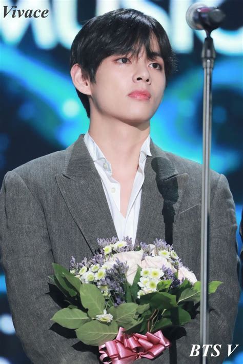 The Young Man Is Holding A Bouquet Of Flowers In Front Of A Microphone