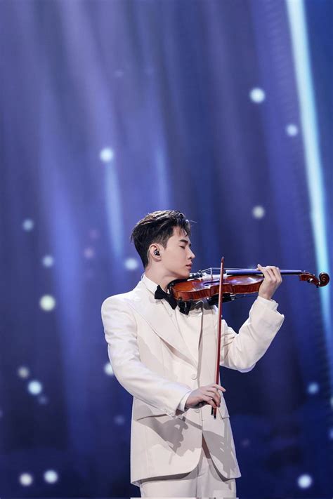 A Man In A Tuxedo Playing The Violin On Stage With Lights Behind Him