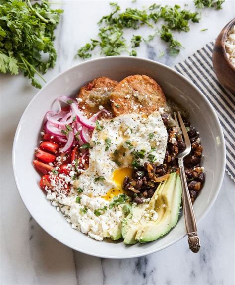 A White Bowl Filled With Eggs Beans And Veggies Next To A Fork