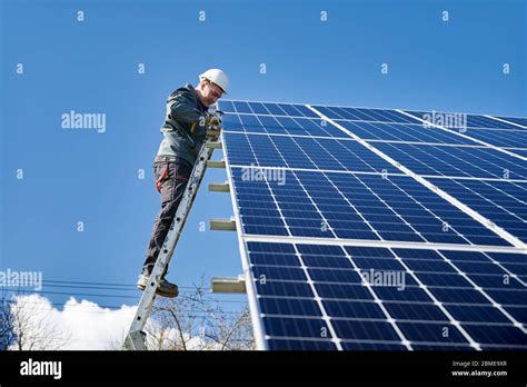 Electrician On Ladder Installing Photovoltaic Solar Panel Under Blue