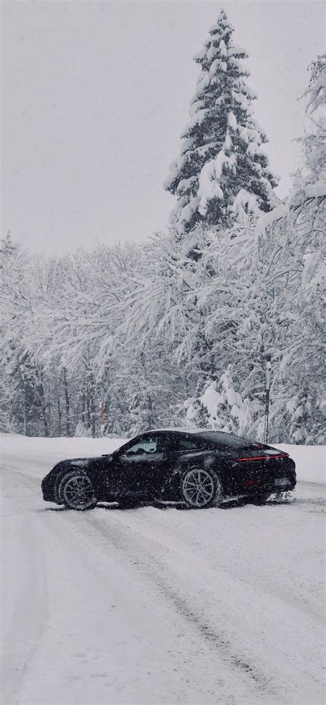 A Black Car Driving Down A Snow Covered Road In The Middle Of Winter