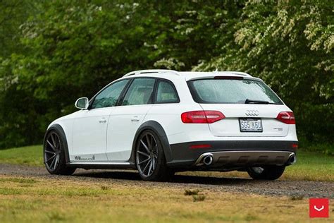 The Back End Of A White Car Parked On A Dirt Road In Front Of Trees