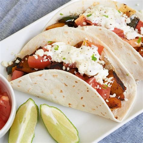 Three Tacos On A Plate With Salsa And Avocado Wedges Next To It