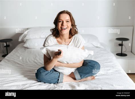 Attractive Young Woman Sitting On Bed At Home Watching Tv Laughing