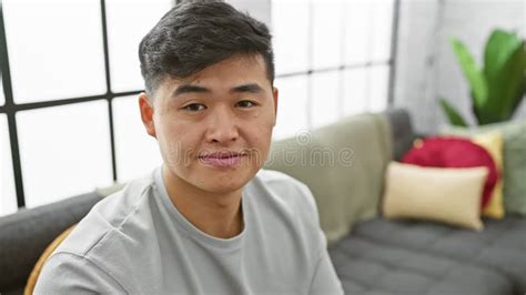 A Thoughtful Young Asian Man Sits In A Modern Living Room Contemplating Alone Stock Video