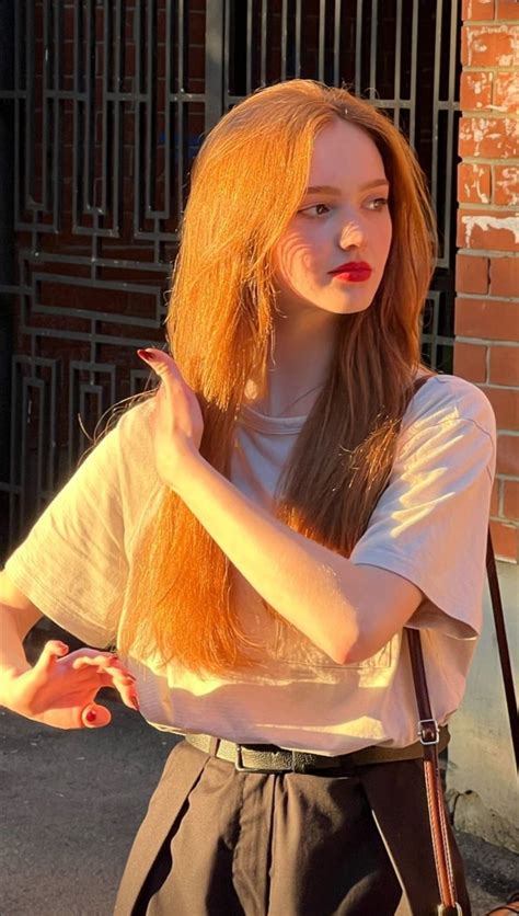 A Woman With Long Red Hair Standing Next To A Brick Wall And Holding A