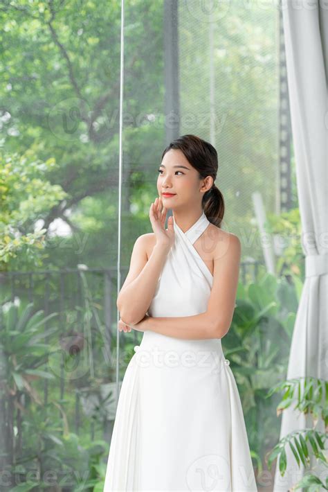 Une Jolie Dame Séduisante Souriant Gentiment Et Vêtue D Une Robe Blanche Se Repose à La Maison