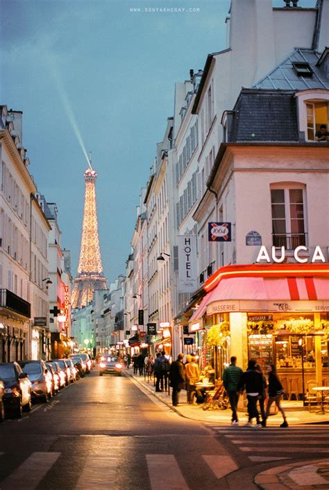the eiffel tower is lit up in the distance as people walk down the street