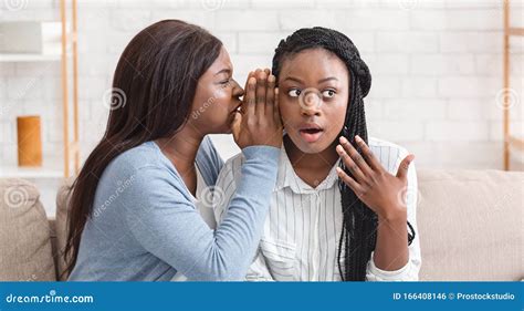 Young Black Girl Whispering Secret To Her Shocked Friend`s Ear Stock