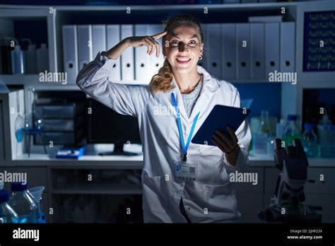 Beautiful Blonde Woman Working At Scientist Laboratory Late At Night Smiling Pointing To Head