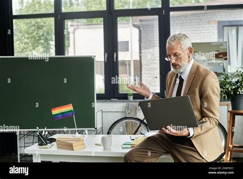 A Mature LGBTQ Teacher With A Beard Teaches Online Through A Laptop In
