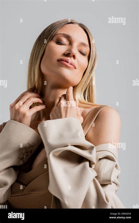 Portrait Of Smiling Blonde Woman In Formal Suit Touching Her Chin On Grey Background Fashion