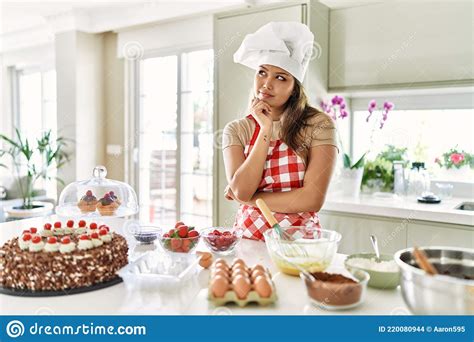 Beautiful Young Brunette Pastry Chef Woman Cooking Pastries At The Kitchen With Hand On Chin